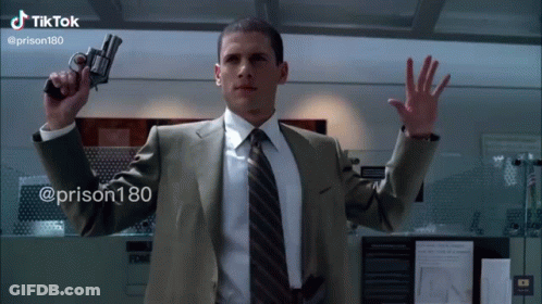 A Man In A Suit And Tie Is Holding A Gun In His Right Hand .. GIF