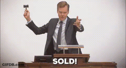 A Man In A Suit And Tie Is Holding A Hammer In Front Of A Podium That Says Sold . GIF