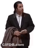 A Man In A Suit And Tie Is Holding A Jacket Over His Shoulder And Smoking A Cigarette . GIF