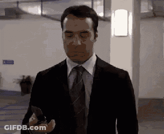 A Man In A Suit And Tie Is Holding A Knife In His Hand GIF