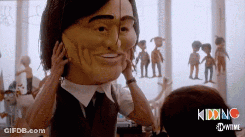 A Man In A Suit And Tie Is Holding A Large Mask On His Face GIF