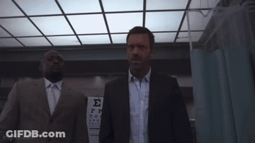 A Man In A Suit And Tie Is Holding A Large Object In Front Of A Sign That Says E. GIF