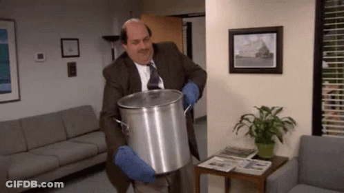 A Man In A Suit And Tie Is Holding A Large Pot In A Room . GIF