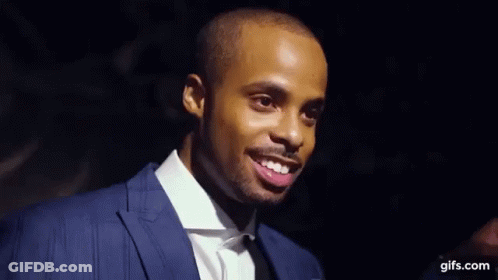 A Man In A Suit And Tie Is Holding A Microphone And Making A Face . GIF