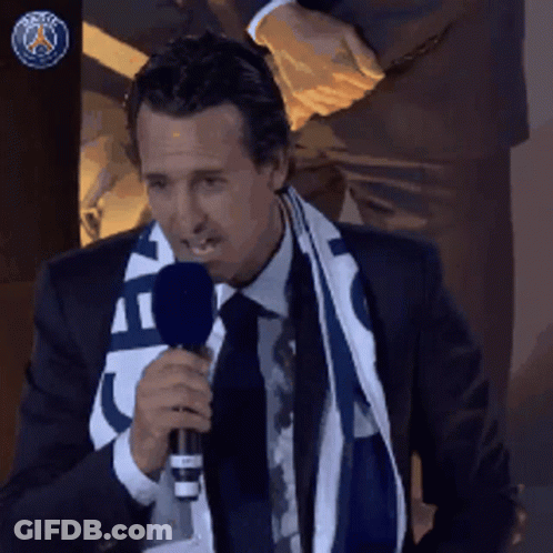 A Man In A Suit And Tie Is Holding A Microphone And Wearing A Scarf That Says Paris GIF