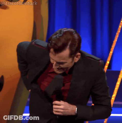 A Man In A Suit And Tie Is Holding A Microphone In Front Of A Blue Curtain That Says Itsscottiesstark On It GIF