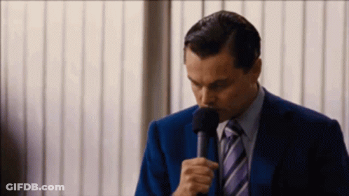 A Man In A Suit And Tie Is Holding A Microphone In His Hand GIF