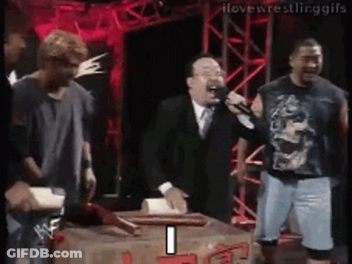 A Man In A Suit And Tie Is Holding A Microphone While Standing Next To A Box . GIF