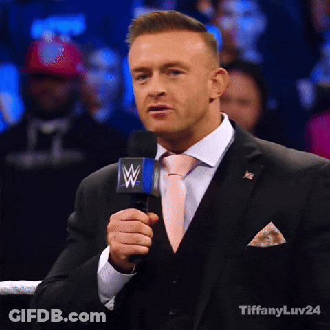 A Man In A Suit And Tie Is Holding A Microphone With A Wwe Logo On It GIF