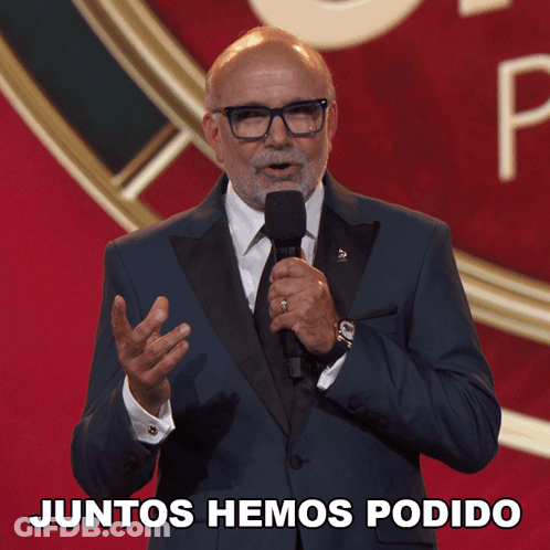 A Man In A Suit And Tie Is Holding A Microphone With The Words Juntos Hemos Podido Below Him GIF