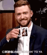 A Man In A Suit And Tie Is Holding A Mug With A Picture Of Him On It . GIF