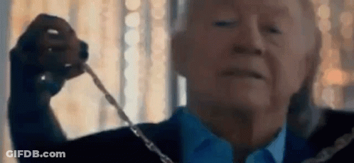 A Man In A Suit And Tie Is Holding A Necklace In His Hand . GIF