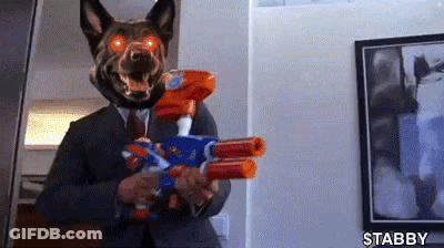 A Man In A Suit And Tie Is Holding A Nerf Gun . GIF