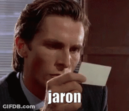 A Man In A Suit And Tie Is Holding A Piece Of Paper In His Hand With The Name Jaron Written On It . GIF