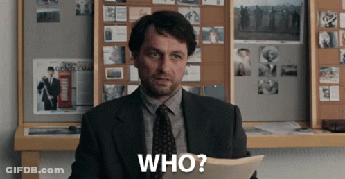 A Man In A Suit And Tie Is Holding A Piece Of Paper That Says Who GIF
