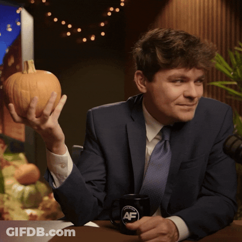 A Man In A Suit And Tie Is Holding A Pumpkin And A Coffee Mug That Says Af GIF