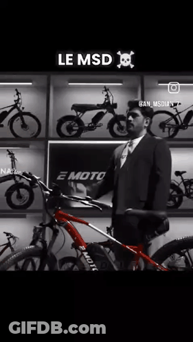 A Man In A Suit And Tie Is Holding A Red Bicycle In Front Of A Wall Of Bikes . GIF