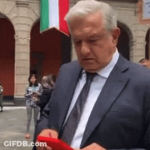 A Man In A Suit And Tie Is Holding A Red Cell Phone . GIF