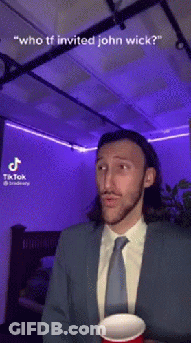 A Man In A Suit And Tie Is Holding A Red Cup And Talking About John Wick . GIF