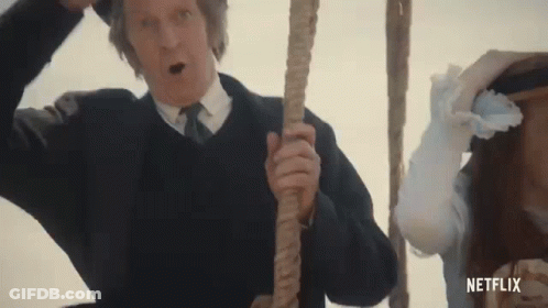 A Man In A Suit And Tie Is Holding A Rope In Front Of A Woman In A White Dress . GIF