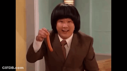 A Man In A Suit And Tie Is Holding A Sausage In His Hand And Pointing At It . GIF