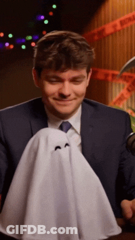 A Man In A Suit And Tie Is Holding A Small Ghost GIF