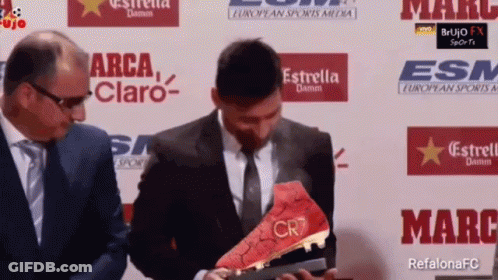 A Man In A Suit And Tie Is Holding A Soccer Boot That Says Cr7 GIF