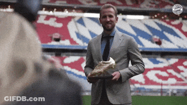 A Man In A Suit And Tie Is Holding A Soccer Boot GIF