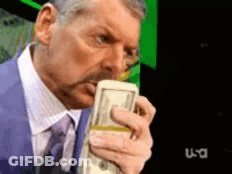 A Man In A Suit And Tie Is Holding A Stack Of Money In Front Of A TV Screen That Says USA GIF