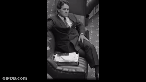 A Man In A Suit And Tie Is Holding A Stack Of Papers GIF