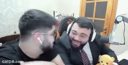 A Man In A Suit And Tie Is Holding A Teddy Bear While Sitting Next To Another Man . GIF