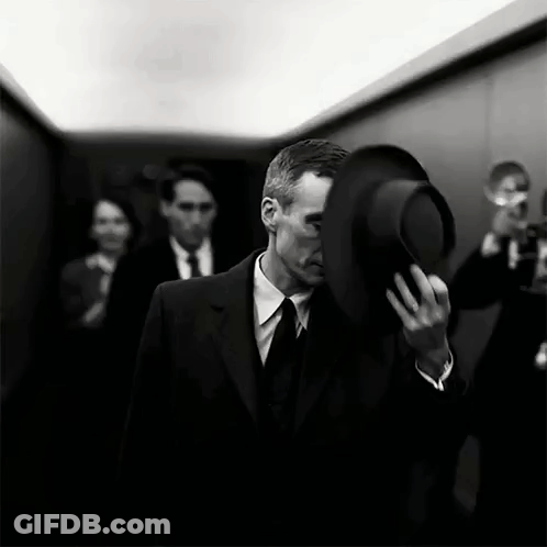 A Man In A Suit And Tie Is Holding A Top Hat Over His Face . GIF