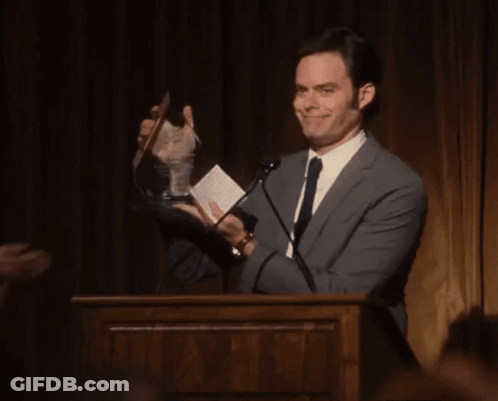 A Man In A Suit And Tie Is Holding A Trophy GIF