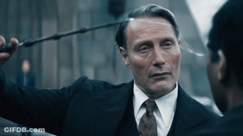 A Man In A Suit And Tie Is Holding A Wand Over His Head GIF
