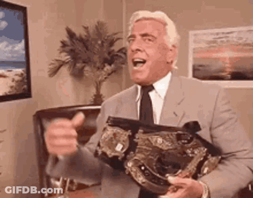 A Man In A Suit And Tie Is Holding A World Heavyweight Championship Belt And Giving A Thumbs Up . GIF