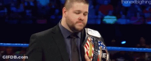 A Man In A Suit And Tie Is Holding A Wrestling Championship Belt In A Ring . GIF