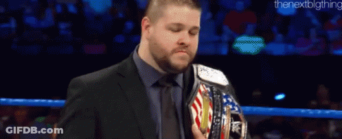 A Man In A Suit And Tie Is Holding A Wrestling Championship Belt In A Ring . GIF