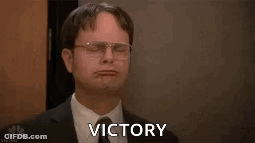 A Man In A Suit And Tie Is Holding His Arms In The Air And Saying Victory . GIF
