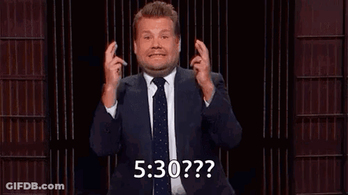 A Man In A Suit And Tie Is Holding His Fingers Crossed And Making A Funny Face . GIF