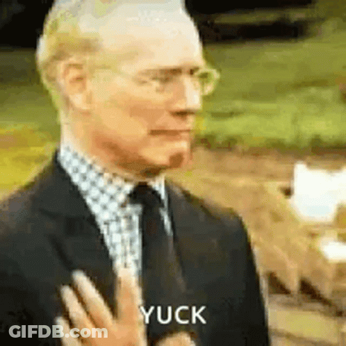 A Man In A Suit And Tie Is Holding His Hand To His Chest And Says Yuck . GIF