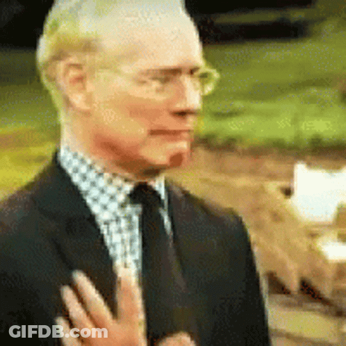 A Man In A Suit And Tie Is Holding His Hand To His Chest . GIF