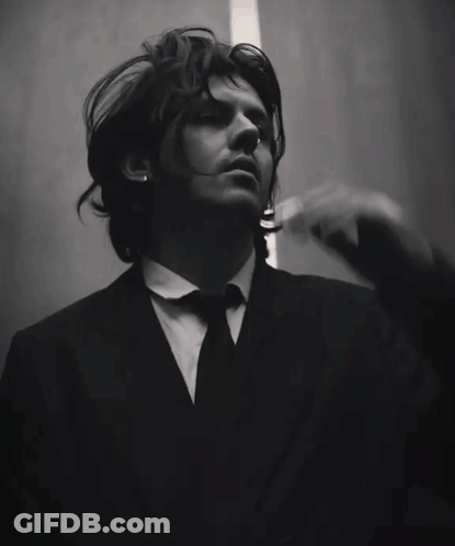 A Man In A Suit And Tie Is Holding His Hand To His Head GIF