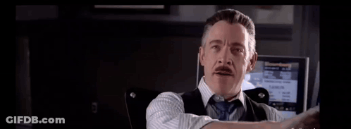 A Man In A Suit And Tie Is Holding His Hand Up In Front Of A Screen . GIF