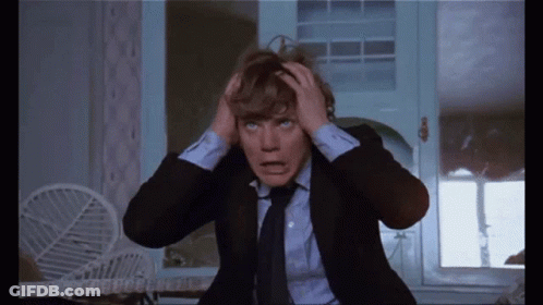 A Man In A Suit And Tie Is Holding His Head In Pain GIF