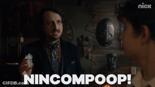 A Man In A Suit And Tie Is Holding Something In His Hand And Says Nincompoop GIF