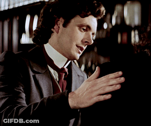A Man In A Suit And Tie Is Holding Something In His Hands GIF