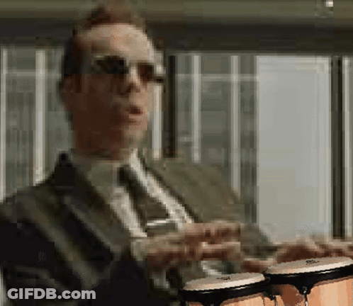 A Man In A Suit And Tie Is Holding Two Bongos In His Hands GIF