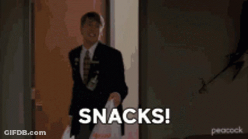 A Man In A Suit And Tie Is Holding Two Plastic Bags And Says Snacks GIF