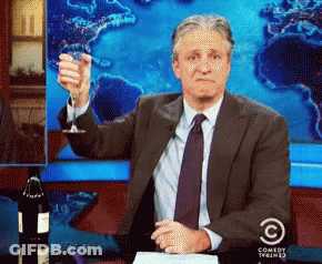 A Man In A Suit And Tie Is Holding Up A Glass Of Wine In Front Of A Comedy Central Logo GIF