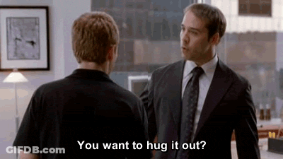 A Man In A Suit And Tie Is Hugging Another Man In A Black Shirt In An Office . GIF